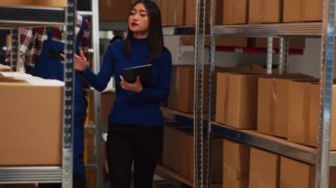 Young adult with crutches analyzing boxes with owner, using tablet to do merchandise logistics in storage room. Asian man talking to entrepreneur about products, physical disability.