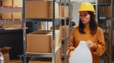 Asian woman presenting warehouse products to man, people working on merchandise quality control in storage room. Young employees looking at goods in boxes, small business plan.