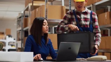 Team of people preparing goods for shipment, checking packages before sending retail store orders. Young man and woman looking at merchandise in packs, storage room shelving. Handheld shot.