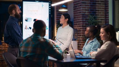 İş arkadaşlarını selamlıyor, iş toplantısında kurumsal sunum yapıyor. Strateji planlaması, finansal analiz raporu tartışma, şirket araştırma istatistikleri görselleştirme. Üçayak atışı.