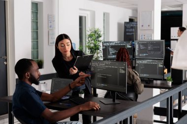 African american web developer using computer to write code and develop algorithm program in big data office room. System engineers working on user interface with html script and terminal window.