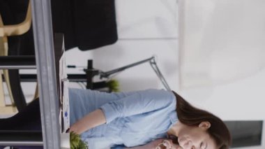 Vertical video: Executive assistant answering landline phone call in startup office, working on business development. Professional manager using office cord telephone to have remote chat at desk.