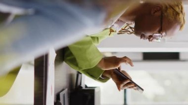 Vertical video: Female employee using mobile phone on work break, navigating on social media app. Executive assistant looking at online browser on smartphone, planning new strategy. Handheld shot.