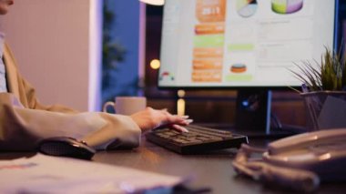 Executive manager checking wristwatch in office, looking at time and working overhours on corporate development. Female worker analyzing financial diagrams on screen, profit growth. Handheld shot.