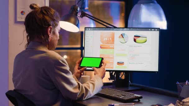 スタートアップオフィスでクロマキーディスプレイを使用して 携帯電話上で水平緑色の画面表示を保持する若い大人 女性従業員は 画面上のコピースペースと隔離されたモックアップテンプレートを分析 — ストック動画
