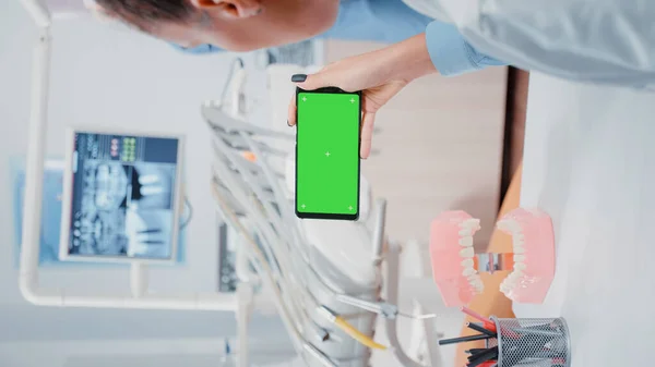 垂直ビデオ 歯科事務所で緑色の画面を持つ携帯電話を見て歯科医 孤立した背景とモックアップテンプレートで作業する女性スマートフォンのための高齢者介護 — ストック写真