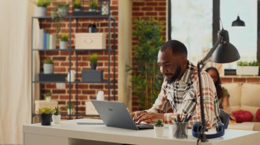 Ofis müdürü evde dizüstü bilgisayarla çalışıyor, dairede ortağıyla oturuyor. Finansal rapor planlamak ve kurumsal e-posta göndermek için bilgisayarı kullanan bir adam, uzaktan masa başında çalışıyor. Üçayak atışı.