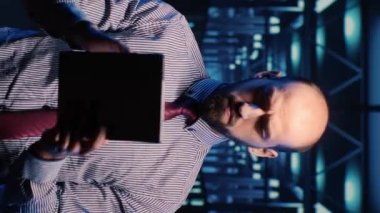 Vertical video: IT manager technical support operator checking big data in server room, planning digitalization. Support specialist working with artificial intelligence and hosting server. Tripod shot