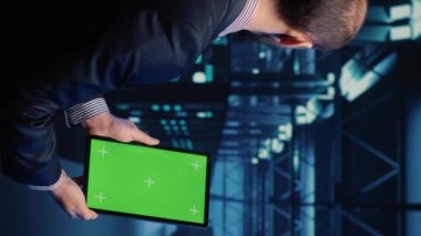 Vertical video: Database admin analyzing greenscreen display on tablet, doing web system check in server room. IT engineer using mockup copyspace display with isolated chroma key. Tripod shot.