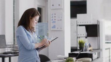 Business manager writing data analytics on papers, working with professional corporate report to increase profit. Young woman taking notes on files for investment plan development.