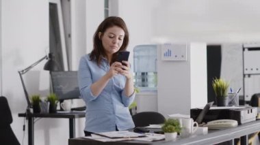 Business worker browsing website on smartphone, using social media app in coworking space. Startup worker taking break from annual report planning with pc, holding mobile phone.