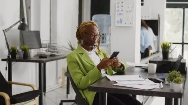 Business manager checking smartphone message at desk, using mobile phone social media app on office break. Young person enjoy scrolling through online browser, career development.