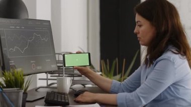 Female manager looking at horizontal greenscreen on mobile phone, working in corporate office with chroma key display. Young woman analyzing smartphone screen with isolated mockup.