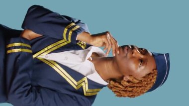 Vertical video: Young air hostess turning on lightbulb with new idea, feeling pensive over blue background. Female airliner in aviation uniform lighting bulb in studio, brainstorming ideas on camera.