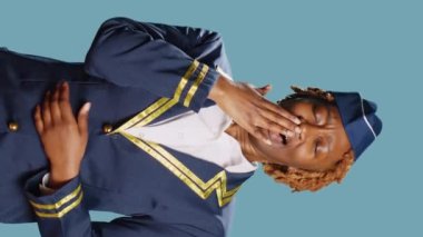Vertical video: African american stewardess yawning in studio, being tired and worn out after commercial flight job. Sleepy air hostess being exhausted and falling asleep, airline crew member.