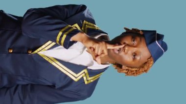Vertical video: African american girl doing mute silent gesture in studio, acting confidential and keeping secret. Young aircrew member dressed in uniform being private and asking for secrecy with