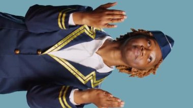 Vertical video: Hopeful stewardess praying to god for good luck, standing over blue background. Young woman working as air hostess showing prayer hands and being wishful, posing on camera.