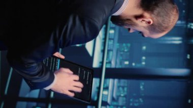 Vertical video: Datacenter engineer using tablet in modern server room, planning cluster computer service or hosting server digitalization. IT manager inspecting system and hardware of data rack