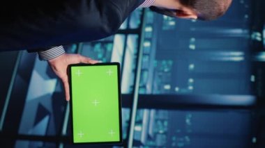 Vertical video: Support specialist using tablet with greenscreen display in modern data center, checking blank chroma key template. Database admin working with isolated mockup and hardware industry