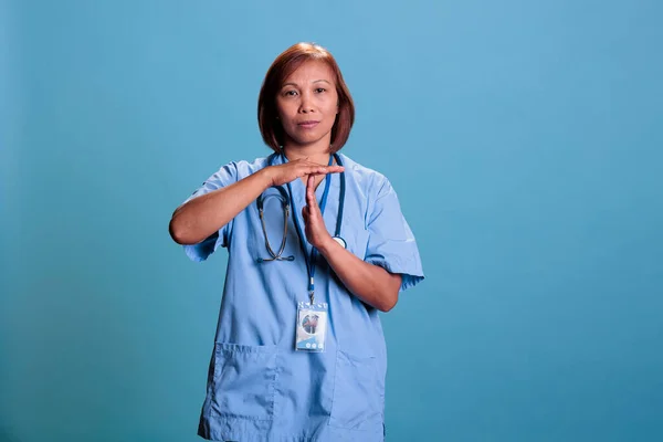 アジアの医療アシスタントは 病気の患者のための医療治療を計画する病気の専門知識で働いている間 手で看板を停止します 真剣な看護師は青の背景を持つスタジオに立って — ストック写真