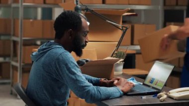 Afro-Amerikalı adam stok ve siparişleri analiz ediyor, depo alanında dizüstü bilgisayar envanteri çıkarıyor. İş planı için lojistik ve mali planlama kullanan erkek çalışanlar.