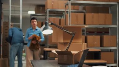 Female entrepreneur taking goods from storehouse racks and putting them in cardboard package, using boxes for shipment. Young adult writing inventory information on laptop, logistics.