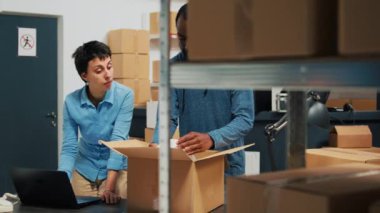 Business owners giving highfive after putting products in cardboard boxes, finishing quality control and delivery logistics. Man and woman feeling cheerful about merchandise distribution.