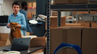 Caucasian woman putting merchandise in packages, working with laptop to do stock inventory before shipping products to customers. Female worker planning delivery management and logistics.