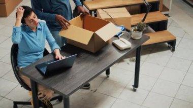 Young entrepreneurs working on goods shipment in warehouse space, putting merchandise from racks in cardboard boxes. Team of partners using products to work on startup development.