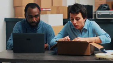 Business owners checking quality of products to ship order from warehouse, using cardboard boxes to pack products. Team of partners shipping merchandise from storehouse. Handheld shot.