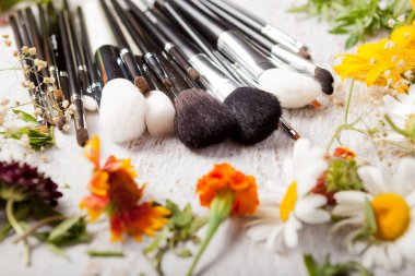 Make up brushes on wooden background next to wild flowers. Professional cosmetics