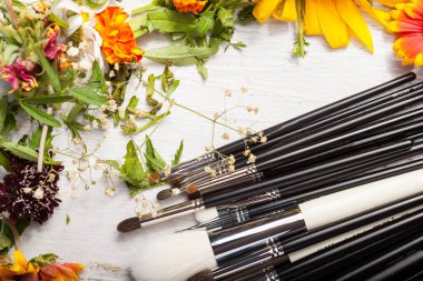 Make up brushes on a table next to wild flowers on wooden background