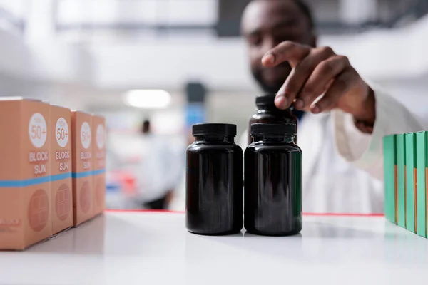 African american pharmacist taking medication from drugstore shelf closeup, selective focus on bottles. Pharmacy medic putting pills close up, vitamins selling, chemist front view