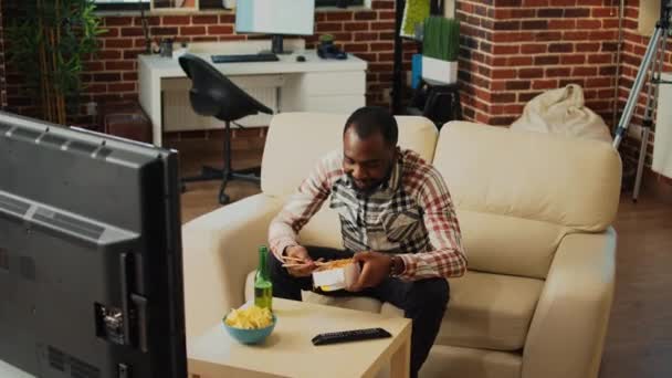 Afro American Mănâncă Tăiţei Sufragerie Stă Televizor Uită Film Tânăr — Videoclip de stoc