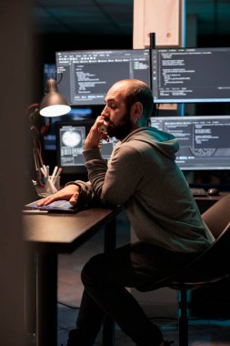 IT engineer answering landline phone call in office, talking about coding html script on cord telephone line. Working late at night to develop new computer system and app servers.