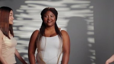 Group of multiracial women smiling for body positivity ad, curvy and skinny friends advertising femininity and body confidence. Girls with different skintones and body types in studio.