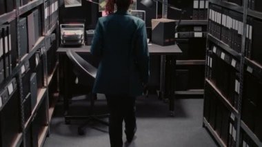African american woman examining evidence map to find suspect, using detective board on office wall. Young police officer analyzing research information for investigation, archive room.