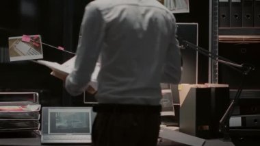 Male inspector analyzing evidence on board in archive room, reading witness statements. Private office looking at suspicious photos and checking criminal records in investigation office.