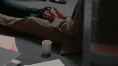 Police archive colleagues reading case information sitting on the floor, working on research to catch suspect. Man and woman doing teamwork to examine detective evidence map. Handheld shot.