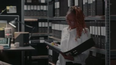 Team of police officers working with case clues on files and laptop, reading witness statements and doing suspect research. Private inspectors examining archive records. Handheld shot.