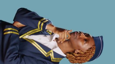 Vertical video: Aircrew member switching on lightbulb with new idea, feeling thoughtful over blue backdrop. Young stewardess in flying uniform lighting bulb on camera, brainstorming ideas in studio.