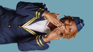 Vertical video: Female aircrew member sending air kisses on camera, acting flirty and cute in studio. Young stewaress dressed in uniform showing romantic sweet gesture, doing kissy face. Aviation job.