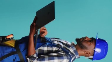 Dikey video: Modern inşaatçı projeye ilham bulmak için dizüstü bilgisayar kullanıyor, internette geziniyor ve kamera üzerinde hesaplamalar veya ölçümler yapıyor. Kablosuz bilgisayarı tutan inşaat işçisi