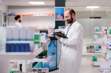 Drugstore employee holding tablet computer checking client prescription while preparing pills order. Pharmacy maintains an inventory of all the different types of pills and medical supplies in stock.