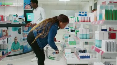 Female customer checking pharmaceutical products from drugstore racks, looking to buy medicaments and supplements for healthcare. Young adult taking medicine and drugs from pharmacy.