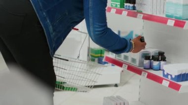 Kadın müşteri, ilaç almak için raflardan sağlık ürünleri alıyor, ilaçlara bakıyor. Genç yetişkin raflarda vitamin ve takviye malzemeleri kontrol ediyor. El kamerasıyla..