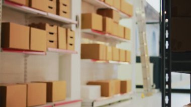 Multiple carton boxes placed on shelves in warehouse, storage room space filled with products and merchandise in packages. Stock distribution and shipment in empty industrial depot. Handheld shot.