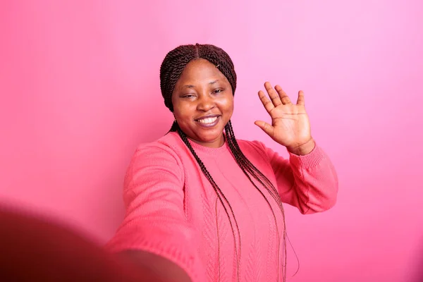 年轻成年人手持摄像机在演播室拍摄自拍的Pov 在演播室举行的视频会议上 一位快乐的女士向远方的朋友致意 粉红背景的模型 — 图库照片