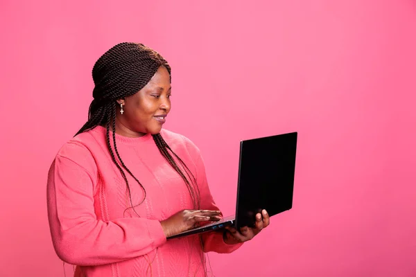 Pembe Tişörtlü Gülümseyen Afro Amerikan Kadın Dizüstü Bilgisayarını Tutuyor Internette — Stok fotoğraf