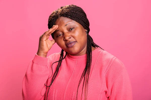 Disgusted young adult putting hand on face after smelling something stinky and disgusting in studio while posing over pink background. Displeased woman being annoying by bad smell